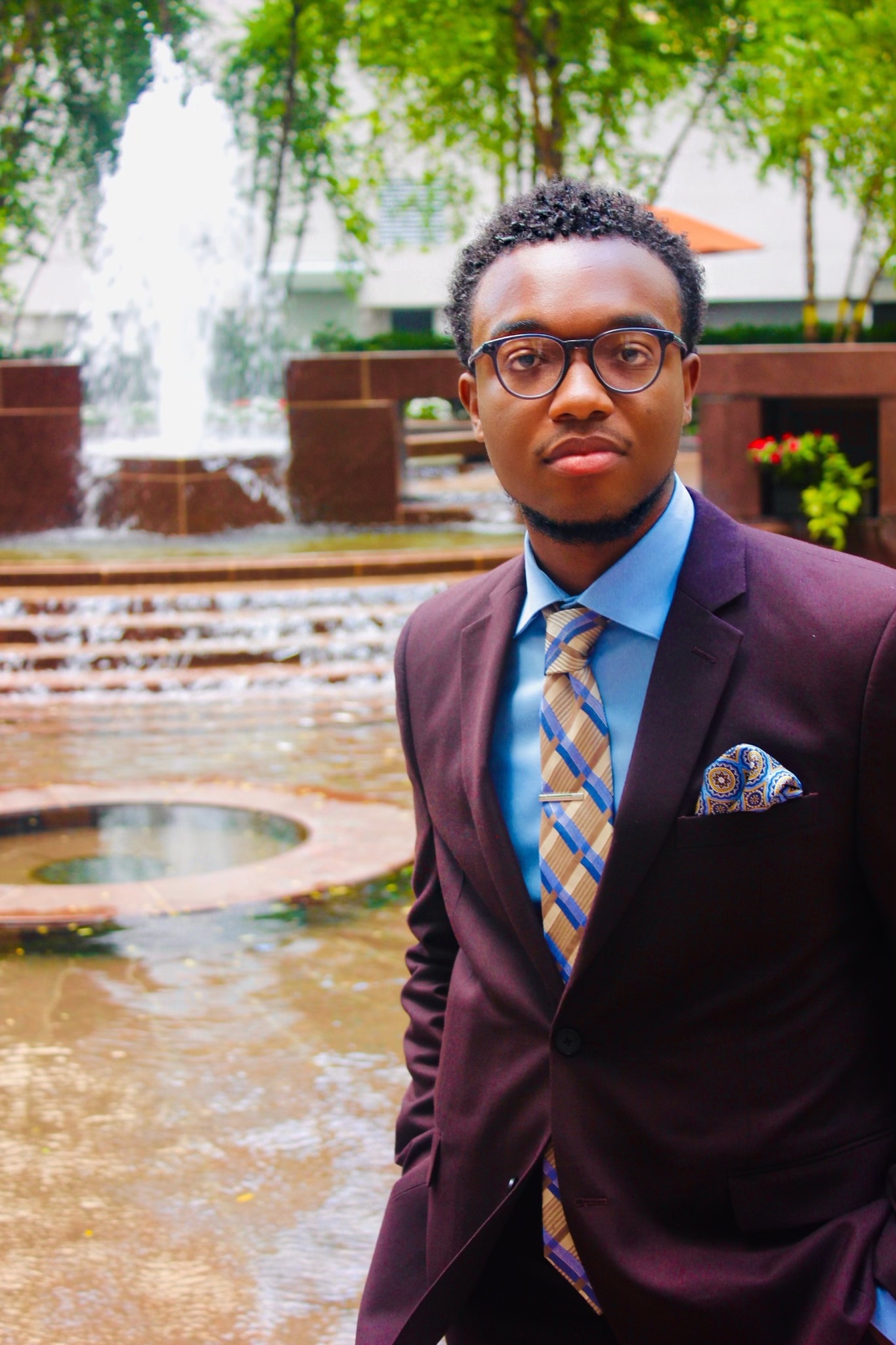 Photo of Christopher Moore LAW '23 wearing a suit and tie standing in front of a fountain.